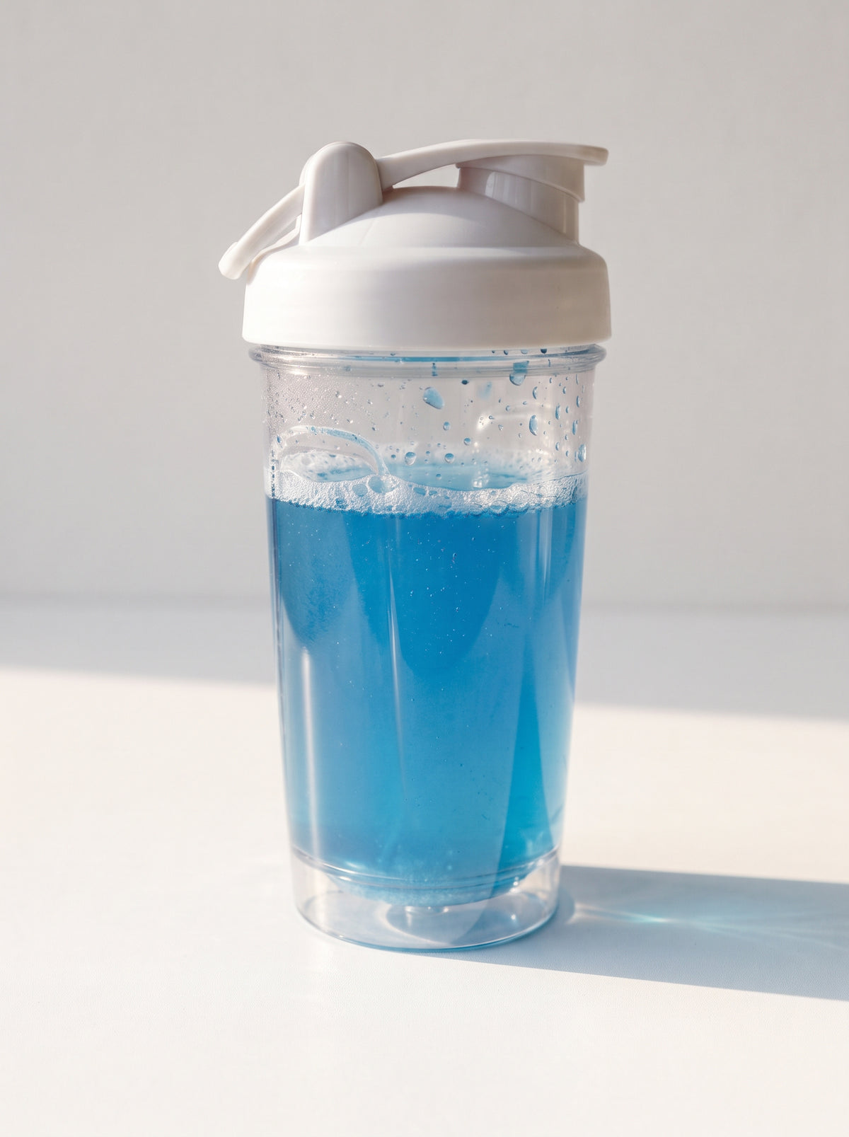 A clear plastic shaker bottle with a white lid, filled with bright blue powder or liquid, set against a clean white background with a soft shadow.