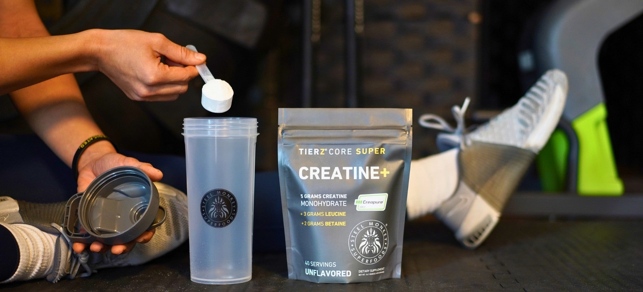 a person sitting on the gym floor scooping creatine into a shaker bottle